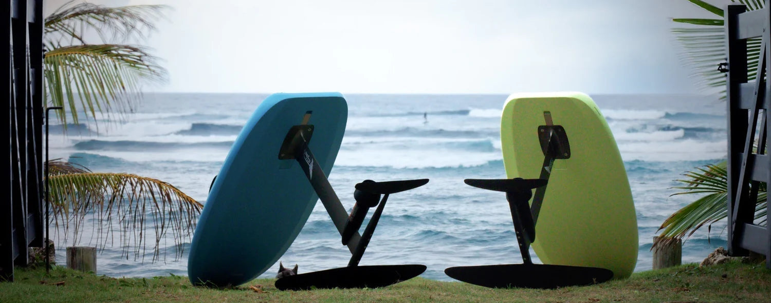 Two surfboards, one blue and one green, leaning against a grassy area with ocean and sky in the background.